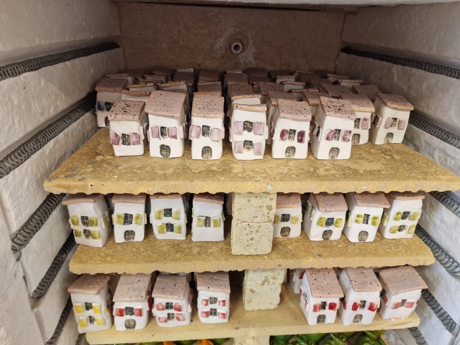 Rows of small handmade ceramic Piran houses with terracotta roofs and coloured shutters, cooling on the shelves of a kiln